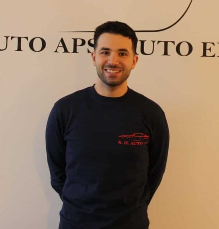 Mand smiler foran K.H. Auto APS væglogo