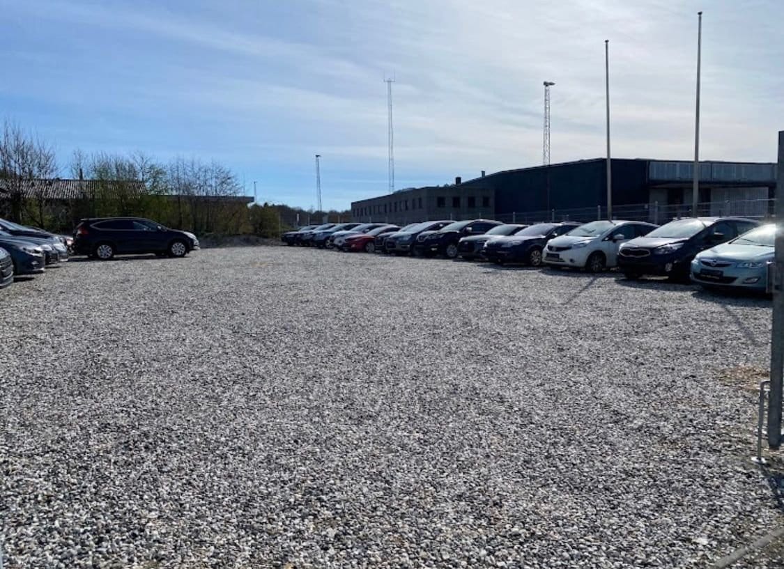 Grusparkeringsplads med parkerede biler ved bygning