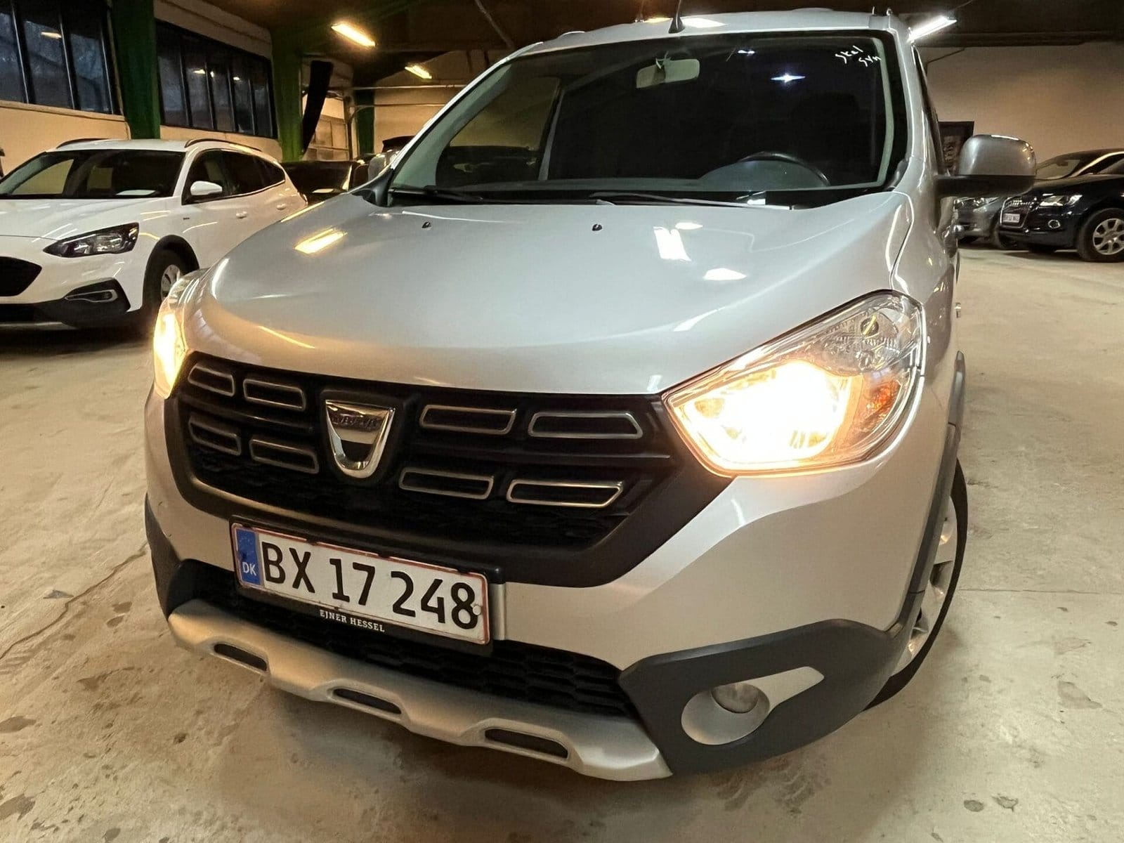 Sølv Dacia bil parkeret indendørs med tændte forlygter